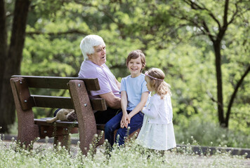 Naklejka na ściany i meble Mature man talking to grandchildren while sitting on bench in park