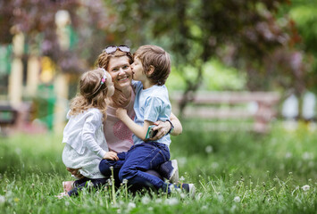Young kids kissing mom while playing in park