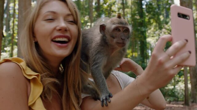 best friends using smartphone taking photos with monkey sitting on shoulder two women having fun posing with monkeys at wildlife zoo tourists travel bali 