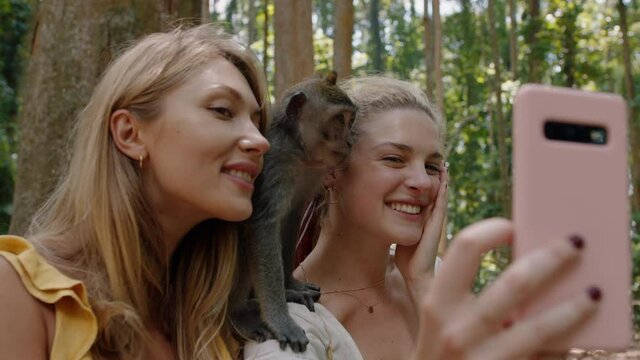 best friends using smartphone taking photos with monkey sitting on shoulder two women having fun posing with monkeys at wildlife zoo tourists travel bali 