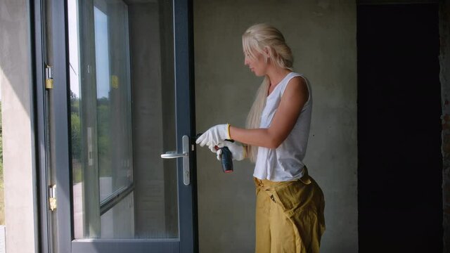 Girl in white gloves twists a screw into a door lock. Repair and installation of a door in a residential building.