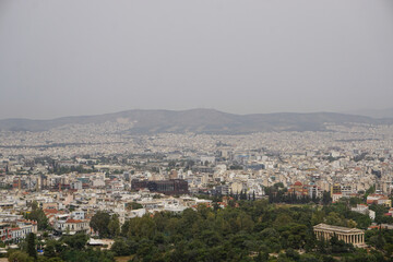 Fototapeta na wymiar Athens, Greece: View from the Acropolis of the Doric Temple of Hephaestus and the Athens skyline, under a hazy sky caused by dust pollution.