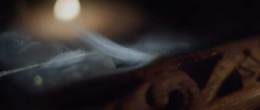 Macro shot of white smoke of incense slowly burning in a wooden holder. Slow motion, shallow depth of field. 