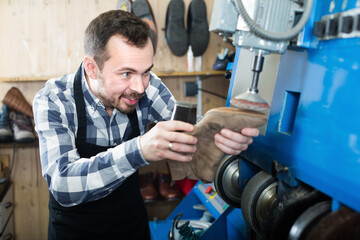 Smiling man worker repairing footwear in repair workplace