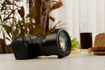 professional camera with lens on a wooden table next to a crystal glass with soda, work tool, art in studio