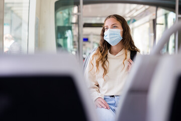 Young european woman in face mask, public transport passenger, traveling in tram