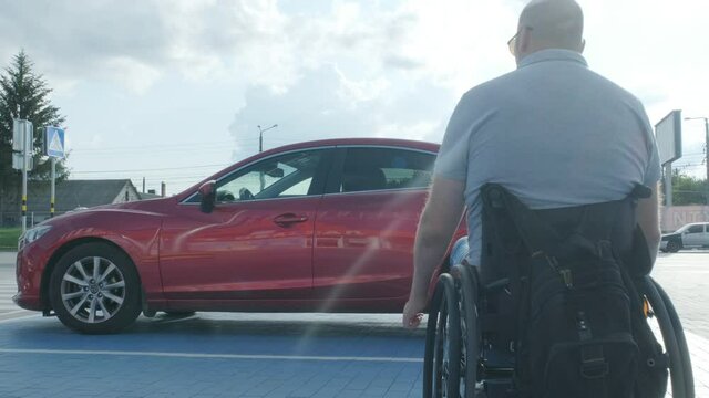 Young handicapped driver getting in red car from wheelchair