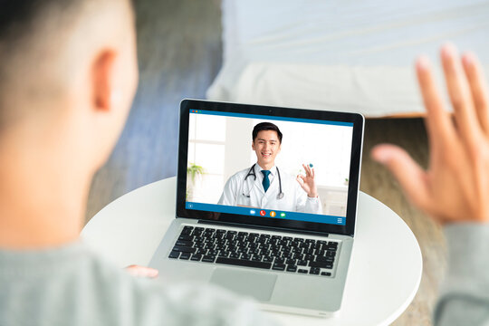 Back view of man talking to dotor by video call with laptop.Dotor smiling and showing ok gesture.