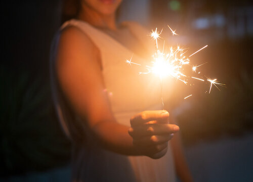 Mujer rubia latina sosteniendo brillante bengala festiva de Navidad en la mano, fuegos artificiales pirot&eacute;cnicos y bokeh en el fondo oscuro para el concepto de celebraci&oacute;n