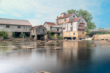 Fototapeta na wymiar A historic mill sits by the glassy waters of a river on a beautiful sunny day in Chisholm, Ontario.