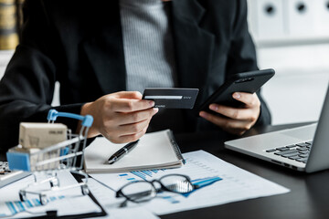 Close up of Businesswomen shopping online on a smartphone with payment via credit card, Accountant doing accounting paperwork and business reports on a desk, e-commerce and business online concept.
