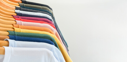 close up collection of color t-shirts hanging on wooden clothes hanger in closet or clothing rack...