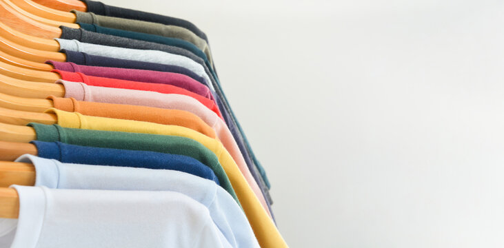 close up collection of color t-shirts hanging on wooden clothes hanger in closet or clothing rack over white background, copy space