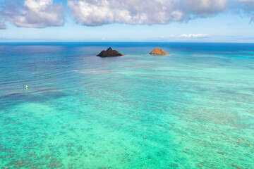 Aerial drone view of the Mokolua islands off the coast of Lanikai Beach in Oahu, Hawaii, USA. Water is turquoise, reef is visible, few white clouds in sky.	