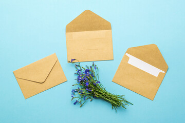 Three paper envelopes for letters and a bouquet of flowers on a blue background. Flat lay.
