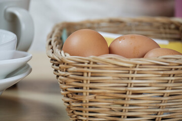 Organic farm-fresh eggs in a woven basket, white cups on a wooden table in the home's kitchen, prepare as an ingredient in the protein breakfast, healthy foods, natural cuisine, and other meal.
