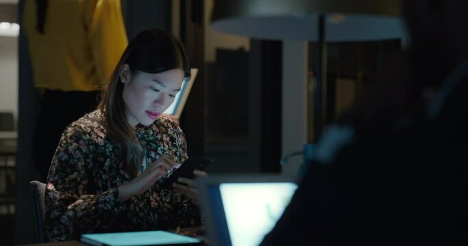 asian business woman working late using laptop computer in office sitting at desk checking smartphone brainstorming ideas browsing on digital tablet technology