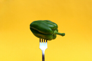 Green pepper is planted on a fork on a yellow background.