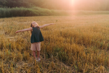 Happy little girl celebrating, holding out her hands in a yellow field. High quality photo