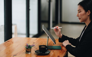 Side view of business woman holding stylus pen pointing on screen of digital tablet on wooden desk