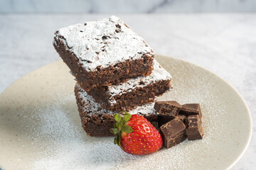 A Batch of Brownies Cut into Squares, arranged from the Left in a Messy Way Close Up, with Crackling Crust on a White Marble Background Shot from Above