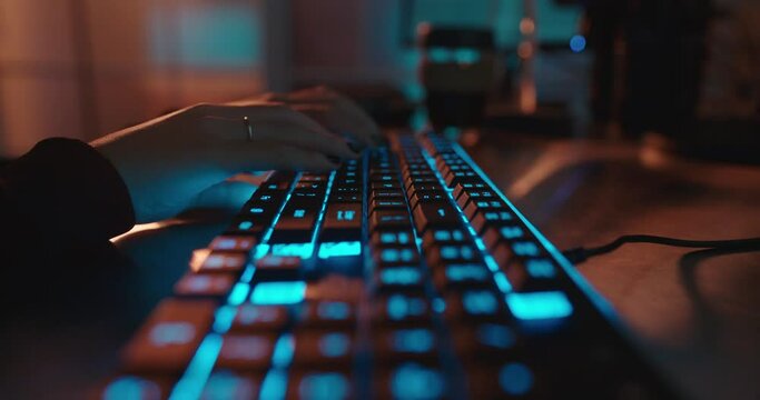 close up hands typing on keyboard programmer coding software gamer using keyboard with blue backlight playing game at night