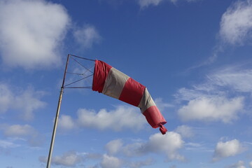 Close up of red and white windsock indicator on blue sky with many white clouds background.