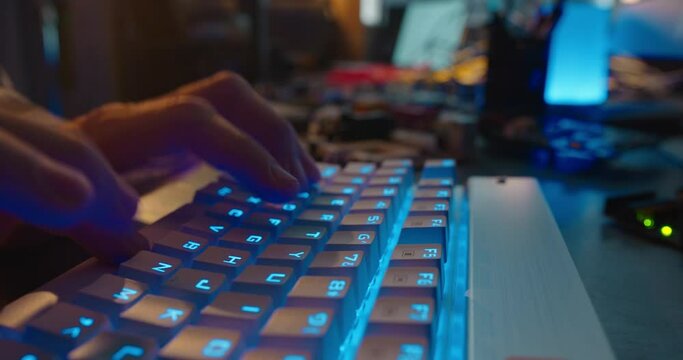 computer hands typing on keyboard browsing online gaming late at night using keyboard with blue backlight