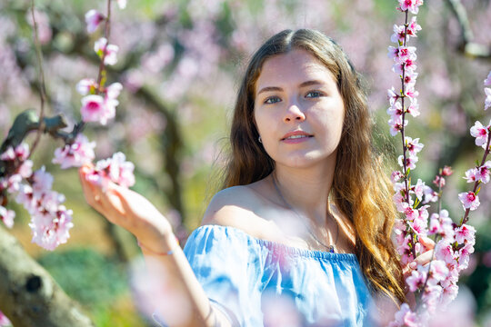 Portrait of young smiling woman in a garden with blooming peach trees. High quality photo