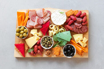 Assorted meat, sausages, cheeses with nuts, olives, croutons on a wooden board. Food on a light background. Top view with copy space. Beautiful serving of snacks. Service delivery, catering.