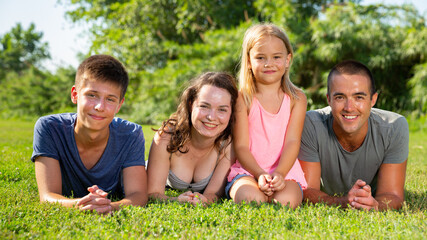 Cheerful friendly family with children gaily spending time outdoors, lying together on green lawn