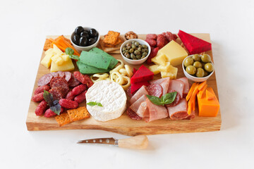 Assorted meat, sausages, cheeses with nuts, olives, croutons on a wooden board. Food on a light background. Top view with copy space. Beautiful serving of snacks. Service delivery, Charcuterie Board.