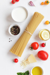 Food ingredients for Italian pasta, spaghetti, fresh farm tomatoes, garlic, peppers, basil, olive oil, Parmesan cheese, lemon, vegetable milk. On white background. Top view with copy space.