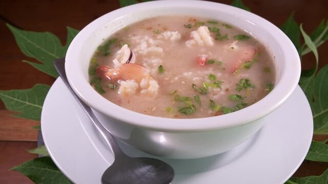An Asian Bowl of Delicious rice soup with Prawns and Shrimp. Thai Breakfast Meal Spinning in a White Bowl