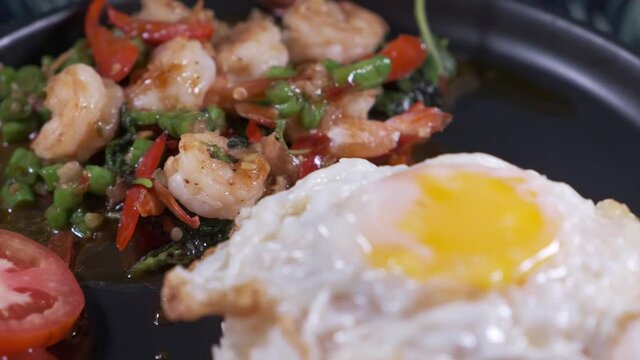 Authentic Thai Spicy shrimp with Basil, Fried Egg and Prawns. Rotating Dish on a Black Plate Close Up.