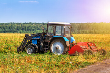 Naklejka premium Modern wheeled agricultural tractor with harvesting equipment on an field