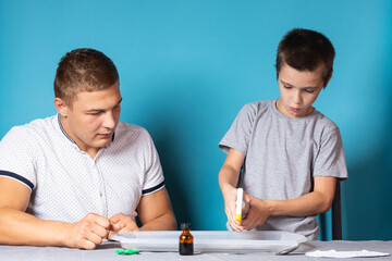 Dad and son are conducting chemical experiments, observing the change in color of a chameleon as a result of the chemical reaction of iodine and starch at home. Boy sprays iodine on a drawing