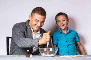 Chemistry education and training concept. Close-up of a boy and his dad doing a home chemical experiment, making slime from glue, sodium tetraborate and dyes