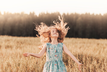 A happy little girl runs through a wheat field in the summer on a sunny day. Summertime. Summer vacation. Happy childhood. Positive emotions and energy