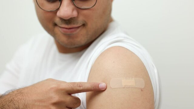 Vaccination campaign.Close up Young indian man getting coronavirus vaccine Immune and showing arm with bandage plaster on isolated white background.
