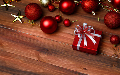 Close up shot of gift present box wrapped with golden ribbon bow placed on old dark wooden table in front glossy shiny decorative hanging balls and star in blurred background with copy space