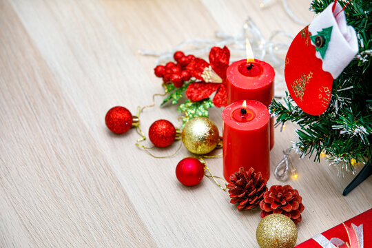 Set of Christmas decorative items red and gold shiny glossy sphere balls Candles Present gift box with silver ribbon bowtie Light bulb rope Pine seeds Xmas mockup tree with hanging sock on wood table