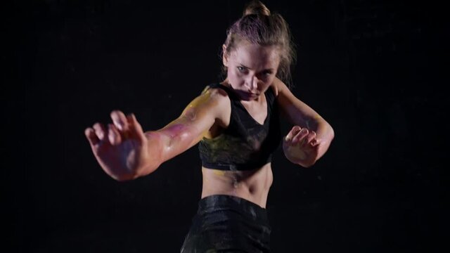 A dancer improvising in a black studio. A woman performing a modern art dance with paint on her skin