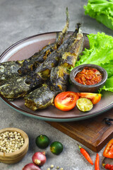 Lele Goreng or Pecel Lele with sambal served with fresh lettuce and tomato. Indoesian food made from fried cat fish. Grey grainy background. 