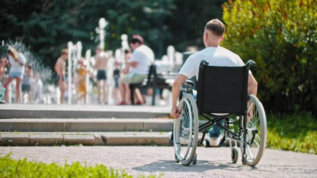 A guy in a wheelchair rides in the park in the summer - sees a ladder and turns away