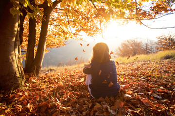 Child sitting in autumn forest in the sunset.