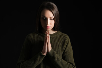 Praying young woman on dark background