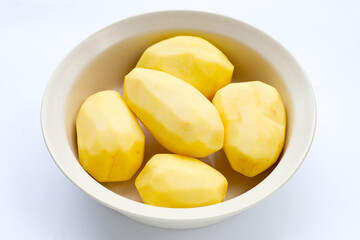 Raw peeled potatoes in white bowl on white background