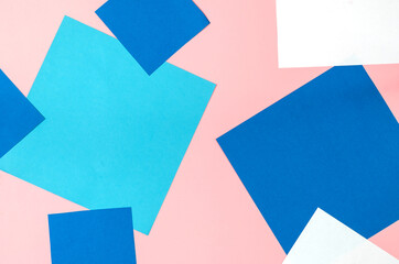 Sheets of colored paper on a pink background. Square blue, white, light blue sheets. Top view.