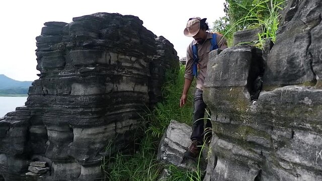 WONOSOBO, INDONESIA - Aug 05, 2021: An HD footage of a man coming down from a rocky hill on a riverbank